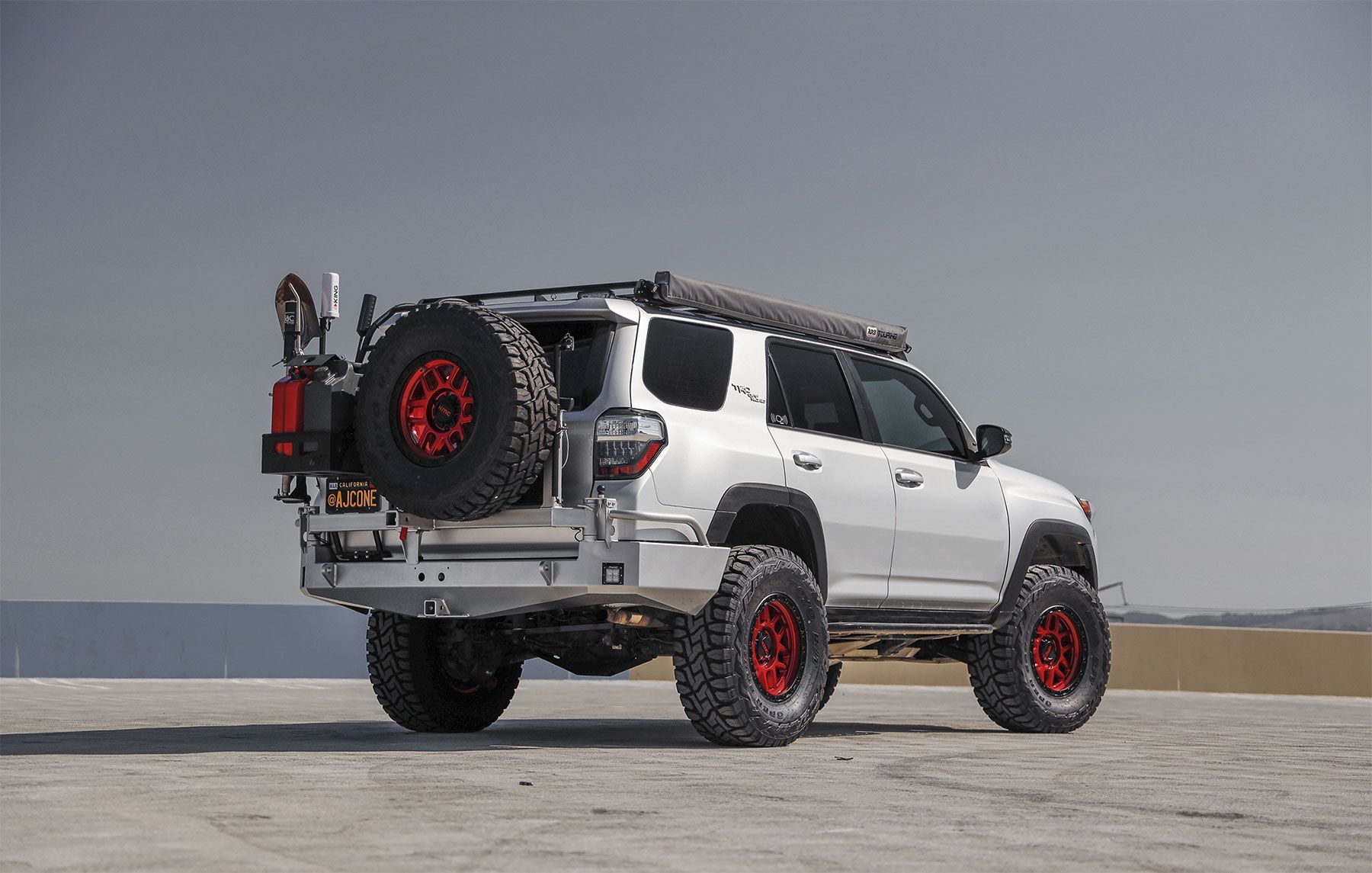 A black jeep with red wheels is parked on a dirt road.